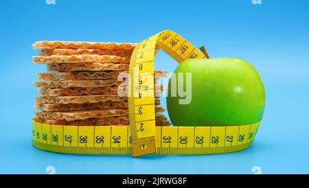 Pile of rye crispbread and green apple on blue background wrapped with yellow measure tape Stock Photo
