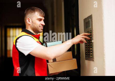 Delivery man pressing button of intercom down the street Stock Photo