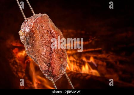 Barbecued Picanha barbecue with blurred fire in the background. Also called churrasco. Stock Photo