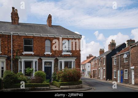 Terraced houses, one with flowering front garden, on St John street and Minster Moorgate all under blue sky in Beverley, UK. Stock Photo