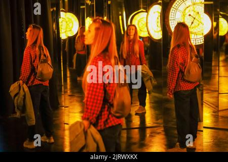 Woman in mirror labyrinth. A woman stands in a mirror maze near a large yellow clock. Blurred image Stock Photo