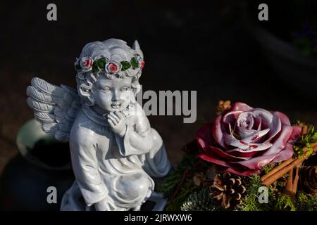 A cute little angel statue with a floral wreath near a rose figurine Stock Photo