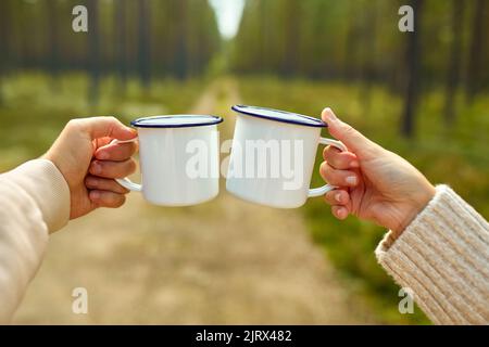 couple clinking white tea mugs in forest Stock Photo