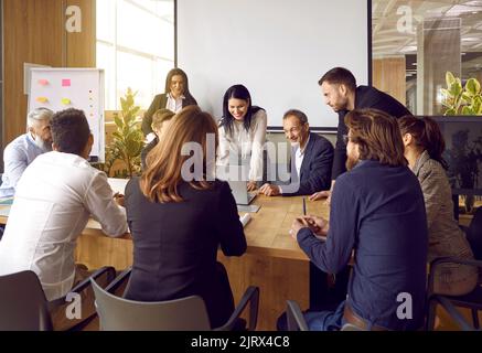 Happy business team gathered at table in office and laughs working together at corporate briefing. Stock Photo