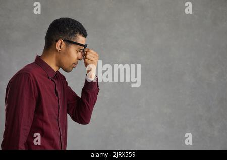 Profile view of a tired dark-skinned young man rubbing his eyes after doing hard work. Stock Photo