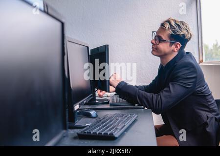 Office worker working hard on his computer. Office full of computers. Programmer working on his computer. Elegant blonde Caucasian man working at a desk. High quality photo Stock Photo