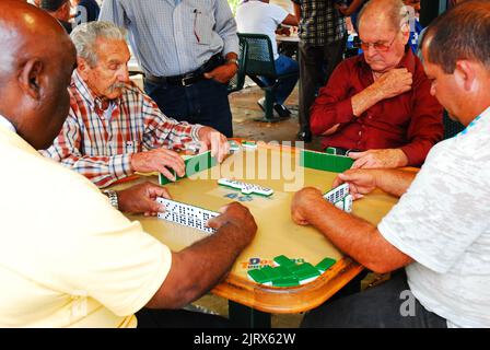 A group of senior men play a friendly game of dominos at a park in the Calle Ocho Cuban neighborhood of Miami Florida Stock Photo