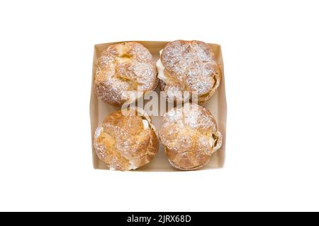 Choux Bun with whipped cream and sugar powder on top in pastry box isolated on white background. Delicate choux pastry dessert. French cream puff. Top view, copy space Stock Photo