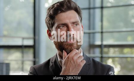 Pensive adult Caucasian bearded man 40s businessman posing looks around thinks pondering pensive thoughtful thinking about job project problem Stock Photo