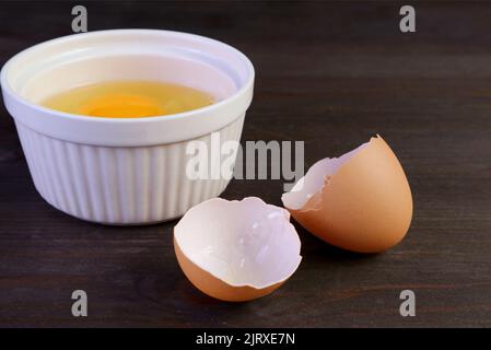 Closeup cracked eggshell on dark brown wooden table with raw egg bowl in the backdrop Stock Photo