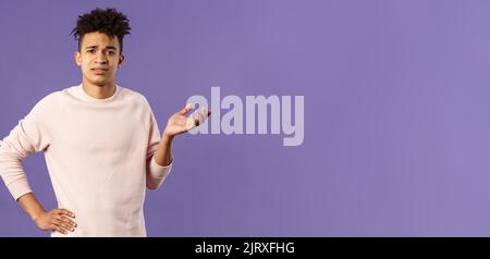 So what, why asking. Portrait of unbothered and careless, ignorant young man dont care on people rules, raising hand in dismay and confusion, being Stock Photo