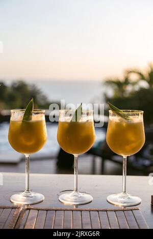 Pineapple cocktail with a green leaf on a bar in front of a swimming pool. Summer vibes Stock Photo