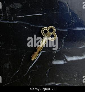 Closeup of a small decorative antique key. On a black marble stone background. Stock Photo