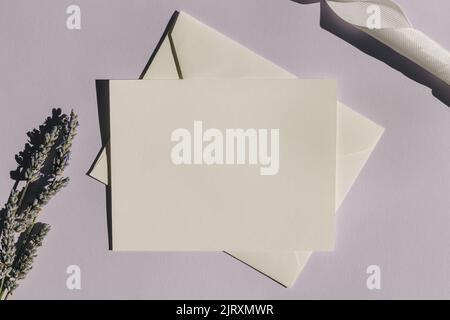 Blank paper card mock-up on pastel purple background with lavender flowers and shadows, top view Stock Photo
