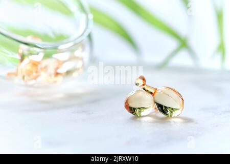 Serum capsules for healthy skin. Blurred background, glass jar with the capsules and green palm leaf. Stock Photo