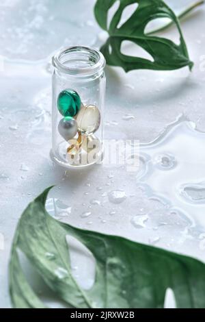 Serum capsules for healthy skin. Blurred background, glass jar with the capsules and green monstera leaf Stock Photo