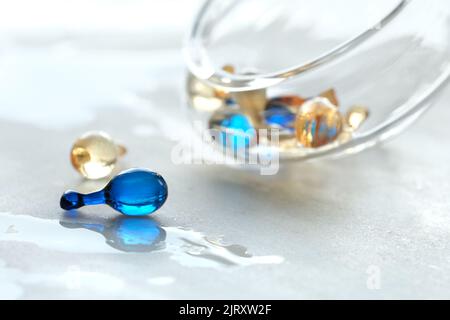 Various serum capsules for healthy skin routine. Blurred background, glass jar with the capsules on wet table. Stock Photo