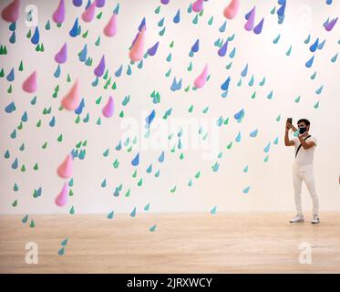 Man wearing face mask takes smartphone photo of colourfull rainrops art installation by Swiss artist Urs Fischer in the Jumex Museum, Mexico City, Mex Stock Photo