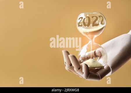 Hourglass, passage of time from 2022 to 2023 year. Wood artistic model hand holding time glass. Countdown to winter holidays. Merry Christmas and a Stock Photo