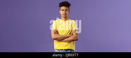 Close-up portrait of skeptical, unimpressed young man with dreads, look judgemental and uninterested, cross arms chest, go on impress me, smirk Stock Photo