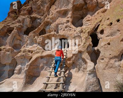 Woman Climbing a Ladder at Talus House, Cliff Dwellings, Bandelier National Monument, New Mexico, USA Stock Photo