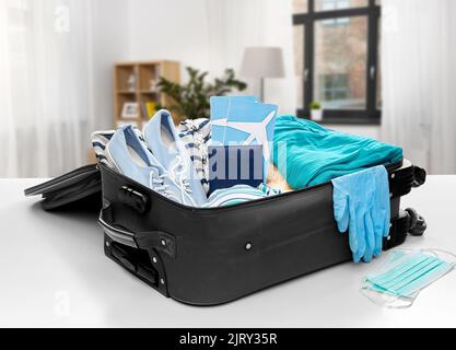 travel bag packed with clothes, gloves and masks Stock Photo