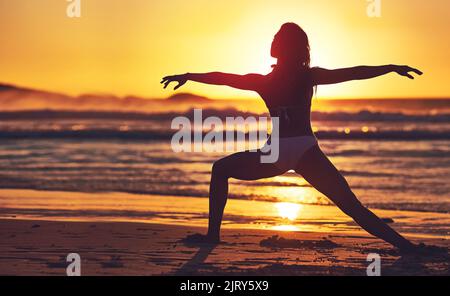 All good things are wild and free. Silhouette of young woman practising yoga on the beach. Stock Photo