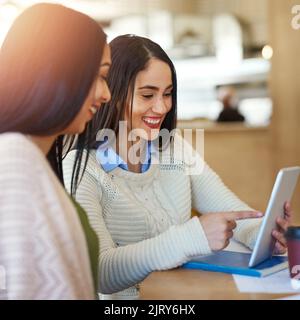 Check out this cat video. two young students using a tablet while studying together in a cafe. Stock Photo
