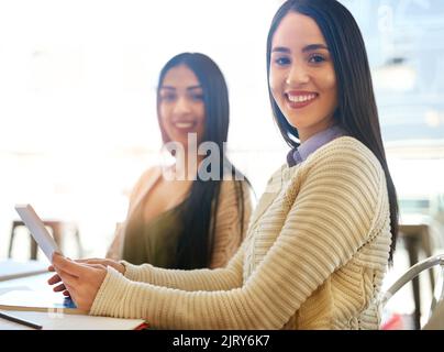 Taking notes has never been simpler. Portrait of two young students using a tablet while studying together in a cafe. Stock Photo