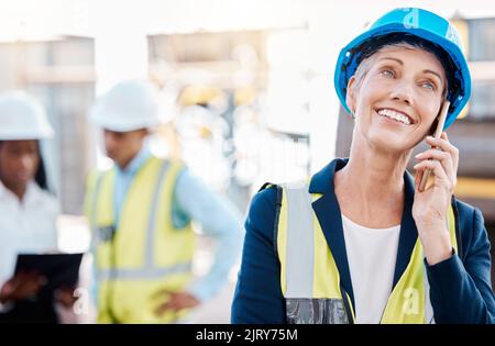 Happy architect talking on a phone call, smiling while standing at a construction site outdoors. Industrial project manager discussing goal and Stock Photo