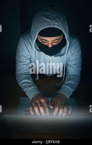 Hell crack that code. High angle shot of a man in a hoodie and mask hacking a computer network. Stock Photo