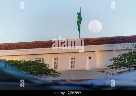 full moon rising beside the flag of brazil on the roof of the copacabana fort in rio de janeiro Brazil. Stock Photo