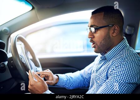 Hes just discovered an app to view real-time traffic updates. a young businessman using a digital tablet while driving a car. Stock Photo