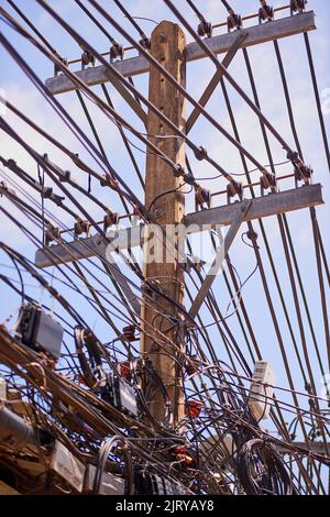 Power running in all directions. chaotic telephone and power cables on a post in Thailand. Stock Photo
