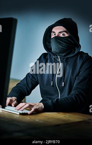 The face of a hardened cyber criminal. Portrait of a young hacker using a computer late at night. Stock Photo