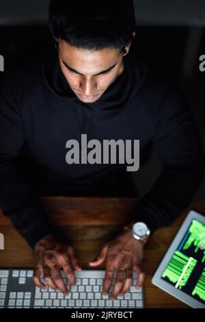 Testing out his latest code. High angle shot of a young hacker cracking a computer code in the dark. Stock Photo