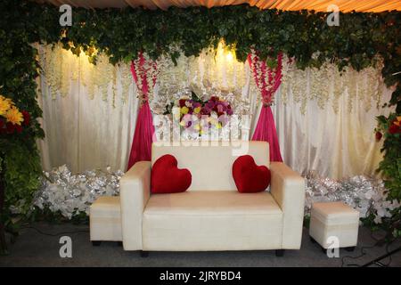 Simple Indonesian wedding chair with two heart-shaped cushions with a lot of flowers and leaves decoration on the back Stock Photo