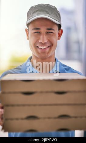From our ovens to your door. Portrait of a happy deliveryman holding a stack of pizza boxes. Stock Photo