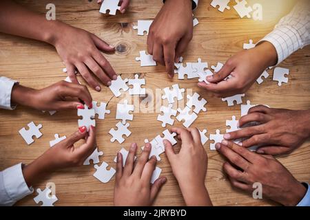 Looking for that perfect fit. High angle shot of a group of unidentifiable businesspeople building a puzzle together in the office. Stock Photo