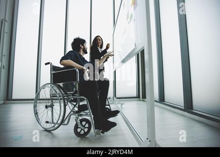 young disabled businessman wearing in wheelchair working and discus with colleague, planning and brainstorming concept Stock Photo