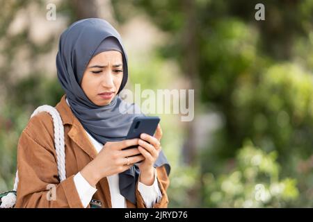 Muslim woman using mobile with a sad expression of disgust Stock Photo