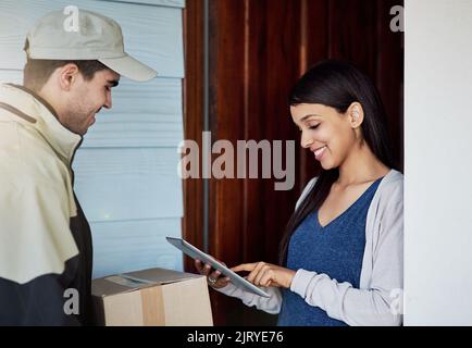 Handling deliveries more efficiently. a young woman using a digital tablet to sign for her delivery from the courier. Stock Photo