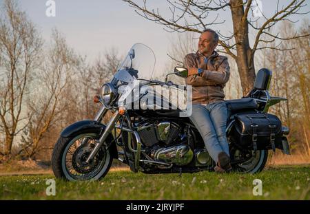 Happy middle-aged man, leaning happily and contentedly on his motorbike, Karlsruhe, Germany Stock Photo