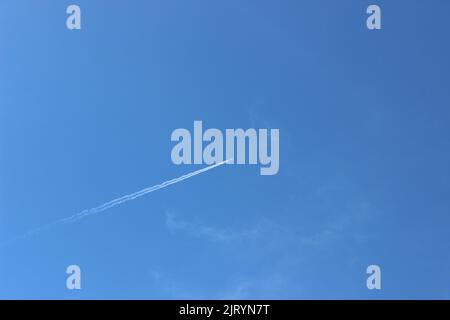The airplane flying in the blue sky leaving contrails from behind Stock Photo