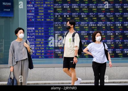 Tokyo, Japan. 24th Aug, 2022. People wearing protective face masks walk past a stock quotation board. Credit: SOPA Images Limited/Alamy Live News Stock Photo
