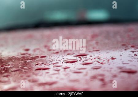 Splashes and water drops on a red car surface forming a beautiful texture pattern background with some parts in focus. Stock Photo
