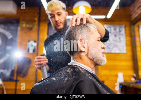 trendy stylish master cuts hair of old man client in modern barbershop Stock Photo