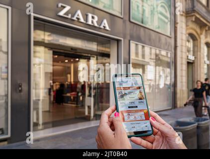 Woman holding a smartphone with the Shein app on the screen and a Zara store in the background Stock Photo