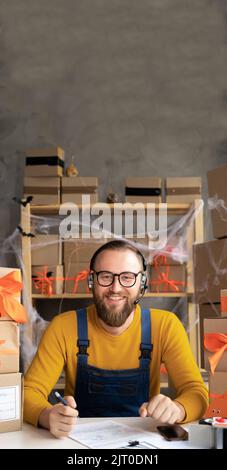 Starting small business entrepreneur taking online order using headphones while sitting at home office on Halloween, dropshipping and goods delivery Stock Photo