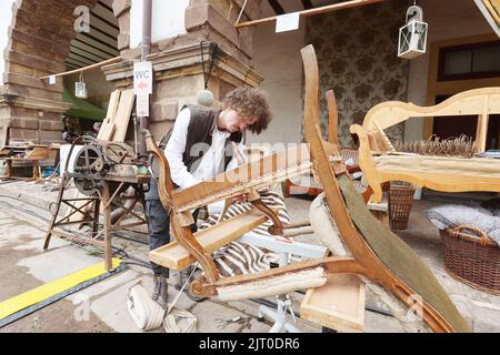 Gotha, Germany. 27th Aug, 2022. Bruce Krämer, journeyman upholsterer, works on a historic chair in the courtyard of the residential palace at the 20th Gotha Baroque Festival. Friedenstein Palace will once again be transformed into the colorful residence of Duke Friedrich III of Saxony-Gotha-Altenburg (r. 1732-1772). Credit: Bodo Schackow/dpa/Alamy Live News Stock Photo